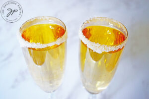 The finished Mock Champagne in sugar-rimmed champagne glasses on a marbled white background.