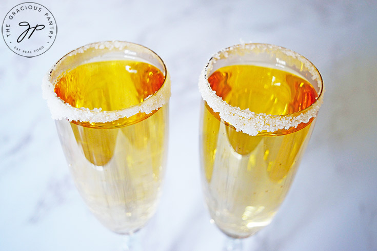 The finished Mock Champagne in sugar-rimmed champagne glasses on a marbled white background.