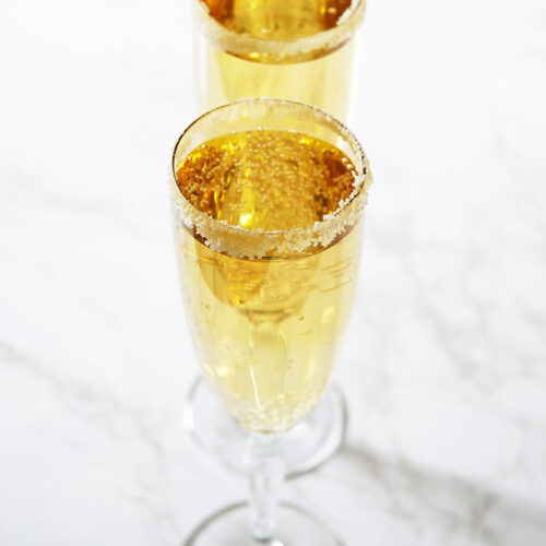 Two champagne glasses in a row, filled with Mock Champagne, on a white background.