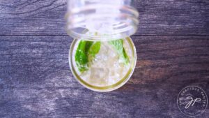 Adding ice to the mojito mocktail in a canning jar.