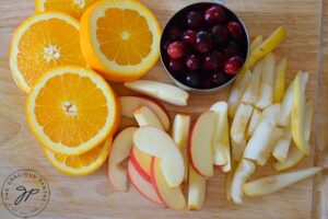 All the fruit for this Non Alcoholic Sangria Recipe, cut and sitting on a cutting board. Oranges, apples, pears and fresh cranberries.