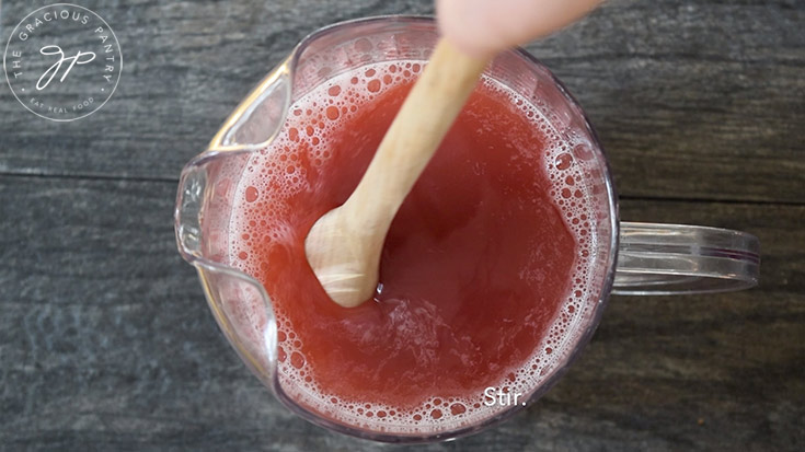 Stirring juice in a large pitcher, with a wooden spoon.