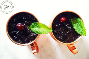 An overhead shot looking down into two copper mugs filled with this Pomegranate Moscow Mule Mocktail Recipe, and garnished with a mint leaf and a fresh cranberry in each mug.