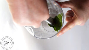 Smashing mint leaves in a clear pitcher with a muddler.