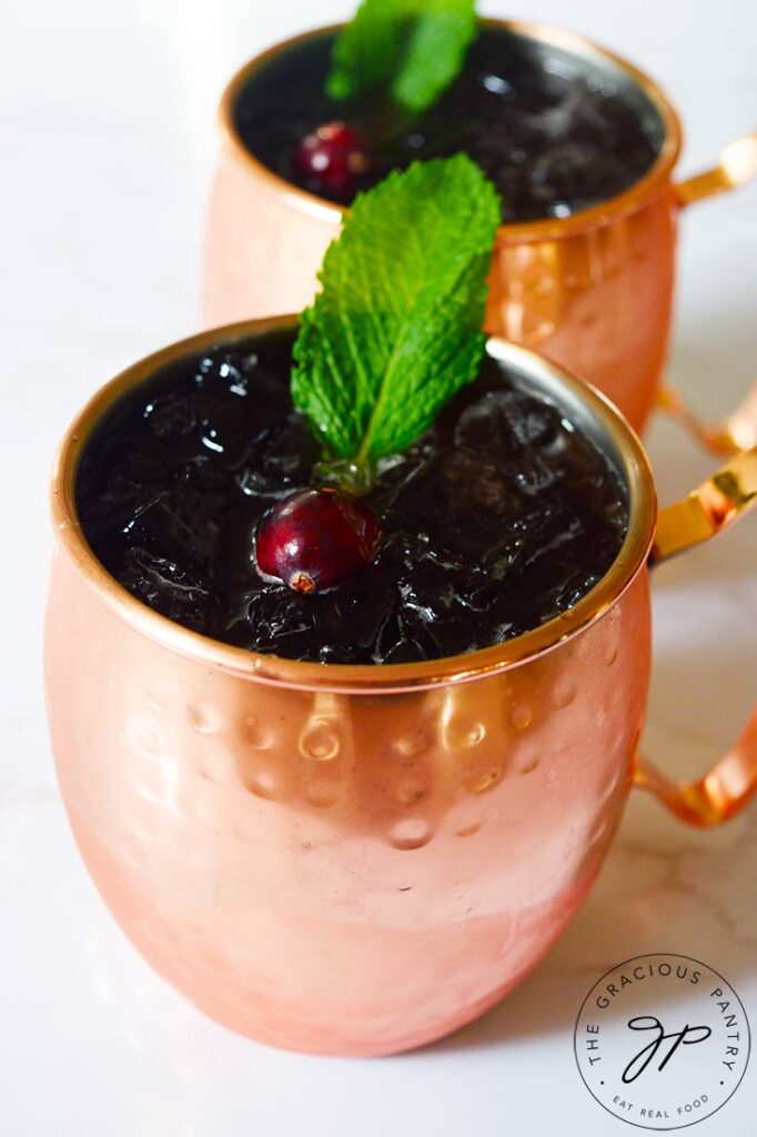 Two copper mugs filled with this Pomegranate Moscow Mule Mocktail Recipe and garnished with a fresh cranberry and mint leaf.