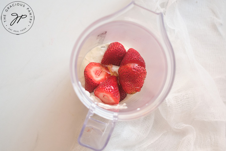 Yogurt, honey and fresh strawberries sitting in a blender cup.