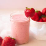 A side view of a small jar filled with Strawberry Smoothie and garnished with a fresh strawberry on the side of the glass.