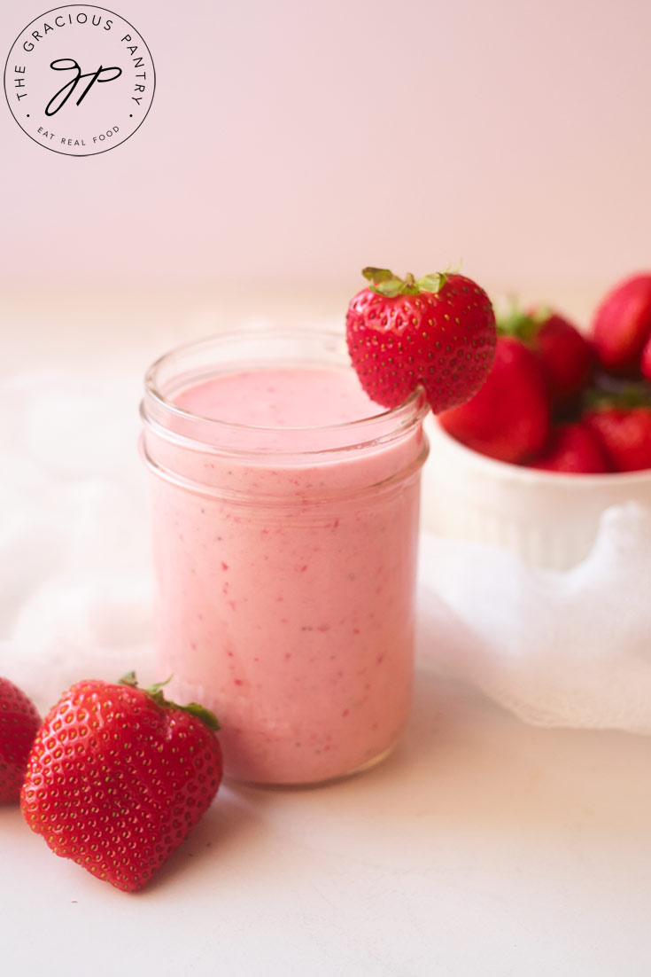 A side view of a small jar filled with Strawberry Smoothie and garnished with a fresh strawberry on the side of the glass.