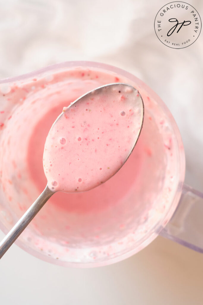 A spoon lifts some of the Strawberry Smoothie out of the blender cup and towards the camera.