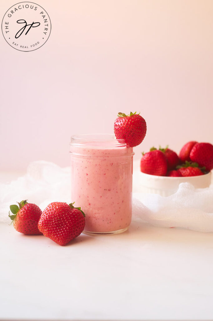 A glass of Strawberry Smoothie, garnished with a fresh strawberry and sitting on a white table.