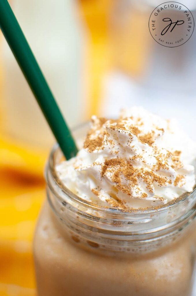 An up close shot of a latte made with Sugar Free Pumpkin Spice Coffee Creamer, topped with whipped cream. A green straw rests in the drink.