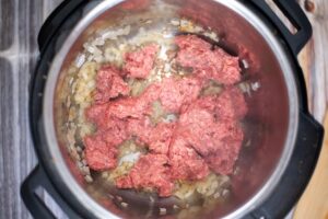 Raw ground beef added to sautéing onions in an Instant Pot.