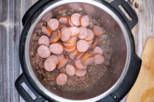 Sliced sausage added to sautéing beef in an Instant Pot.