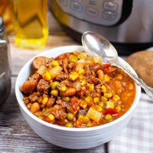 A white bowl filled with this Instant Pot Texas Cowboy Stew Recipe. An Instant Pot sits behind it.