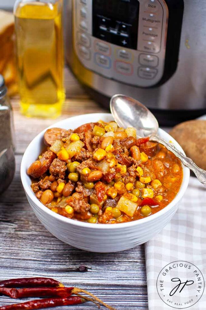 A white bowl filled with this Instant Pot Texas Cowboy Stew Recipe. An Instant Pot sits behind it.