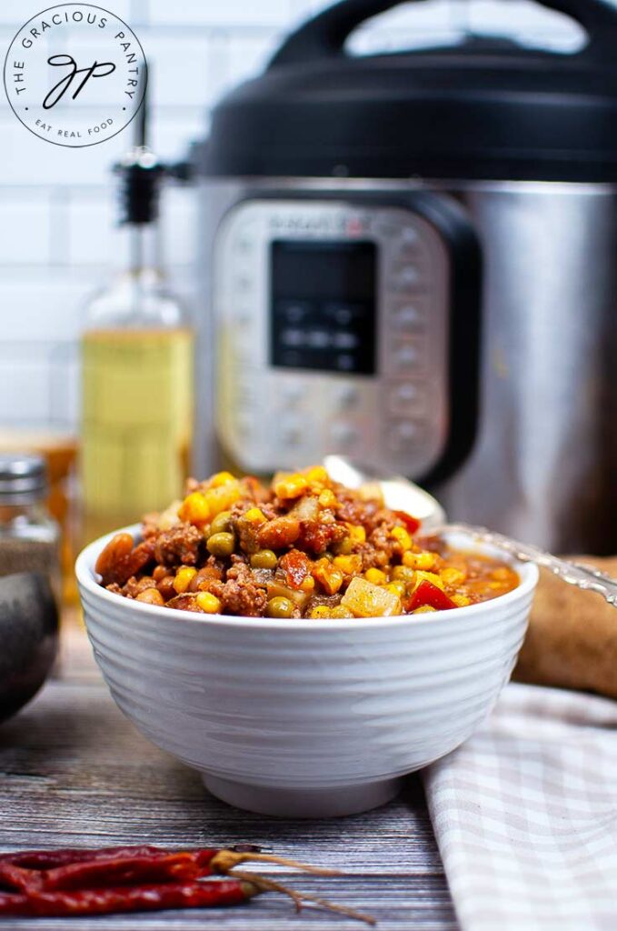 A side view of a white bowl filled with this Instant Pot Texas Cowboy Stew Recipe. An Instant Pot sits behind it to the right, a bottle of oil to the left.