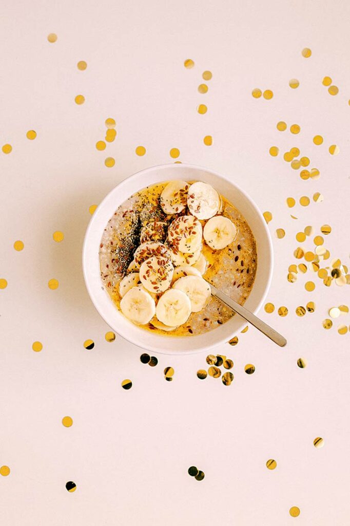 A white bowl of baked banana bread oatmeal topped with sliced bananas and flaxseed.