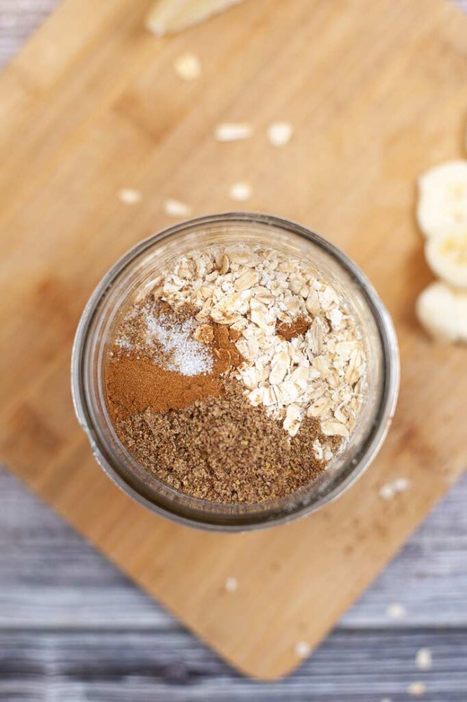 Oats, spices and sweetener added to an open canning jar.