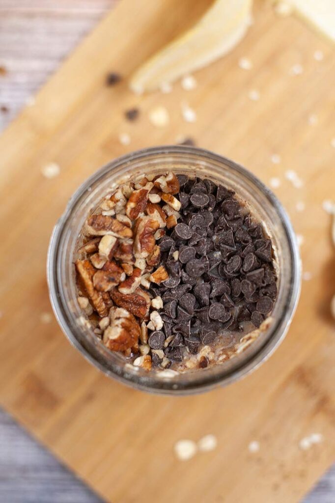 Chopped pecans and chocolate chips added to the oats in an open canning jar.