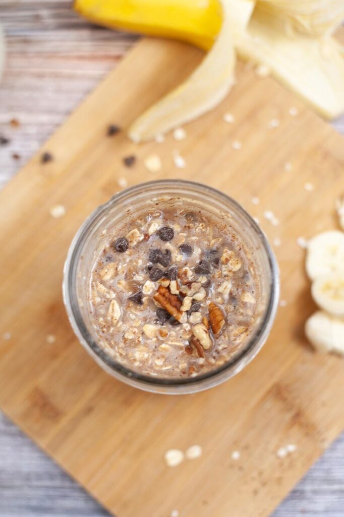 Pecans and chocolate chips stirred into an oat mixture in an open canning jar.