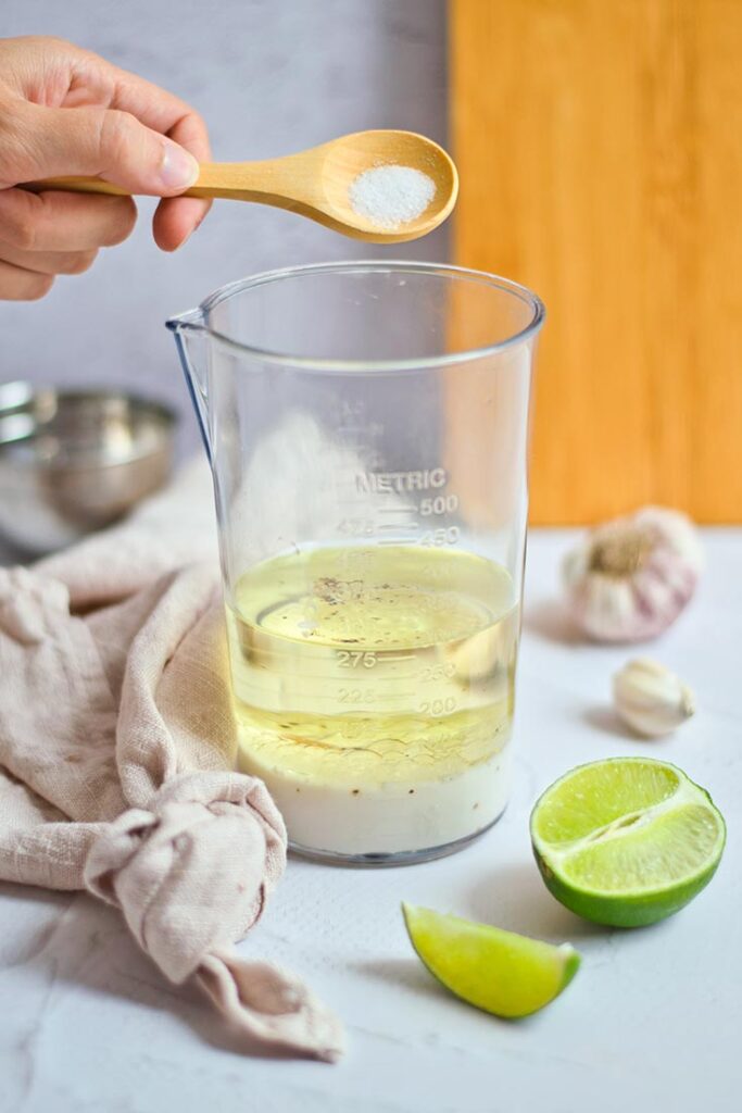 Adding salt to a tumbler of Chipotle Aioli Recipe ingredients for blending.