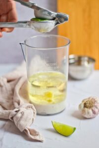 Squeezing fresh lime juice into a tumbler full of Chipotle Aioli Recipe ingredients.