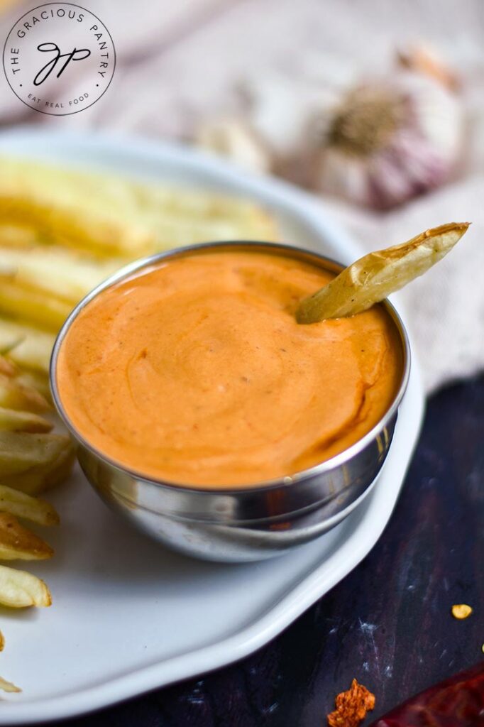 A side view of a small bowl filled with Chipotle Aioli. French fries sit to the left of the bowl.