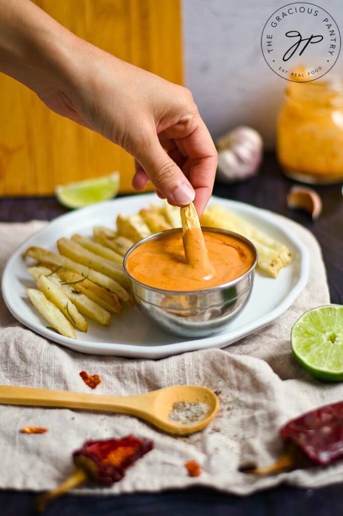 A female hand dips a french fry into a small bowl of sauce.