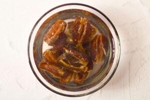 Pitted dates soaking in a clear glass bowl of water.