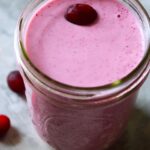 A canning jar glass filled with Fresh Cranberry Smoothie and topped with a fresh cranberry.