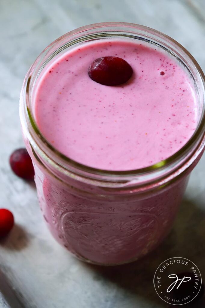 A canning jar glass filled with Fresh Cranberry Smoothie and topped with a fresh cranberry.