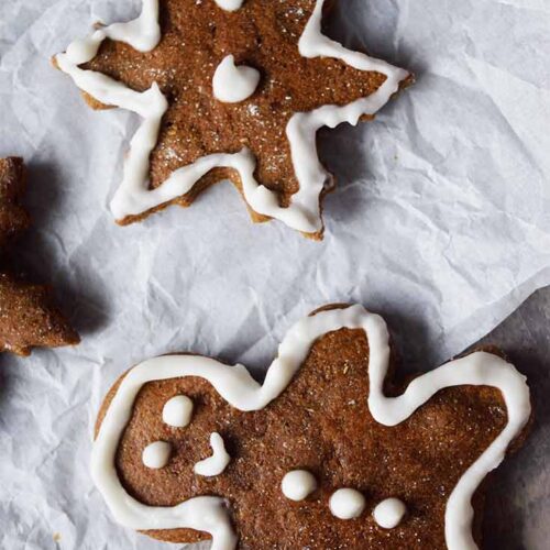 An overhead shot looking down on decorated, healthy gingerbread cookies sitting on white parchment paper.