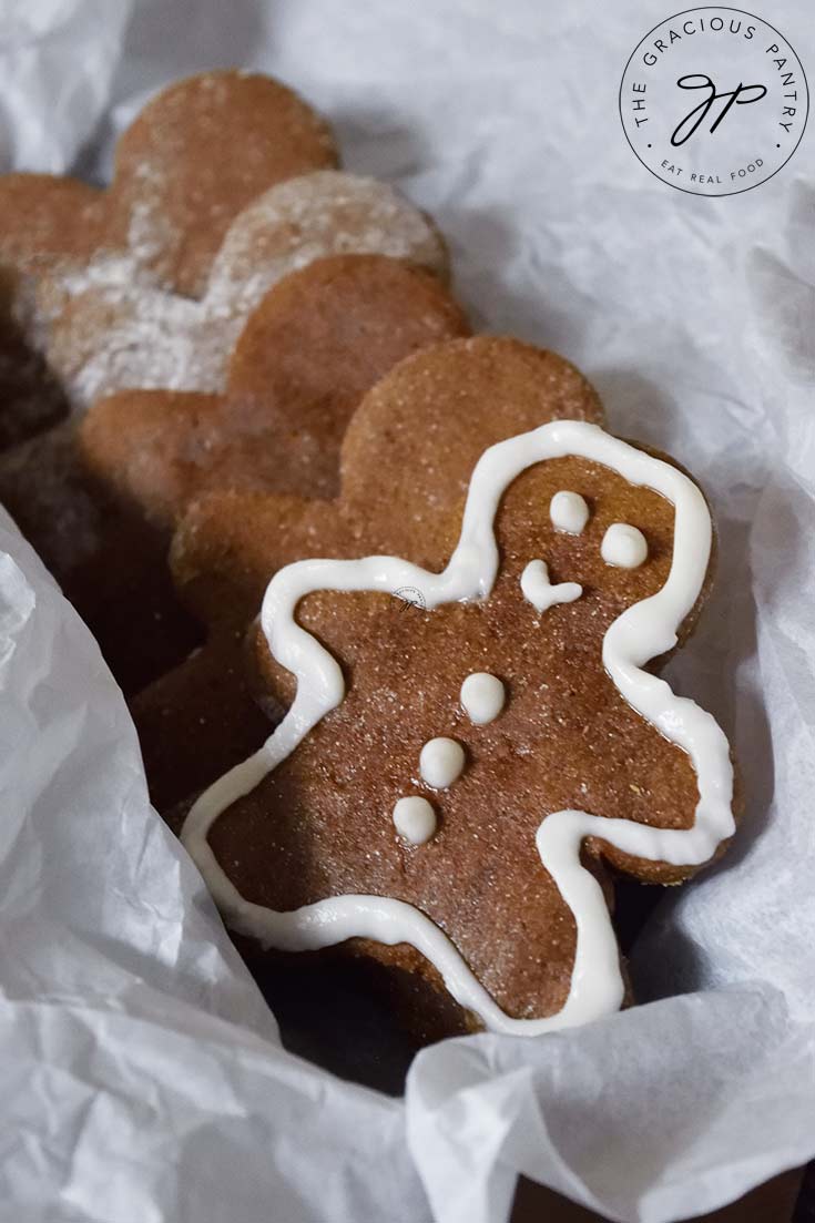 A row of gingerbread man cookies in a parchment lined box. The first cookie is outlined with icing.