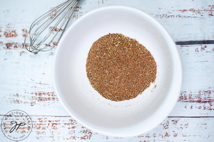 All the spices for this Homemade Fajita Seasoning Recipe blended together in a white bowl. A whisk rests at the side of the bowl.