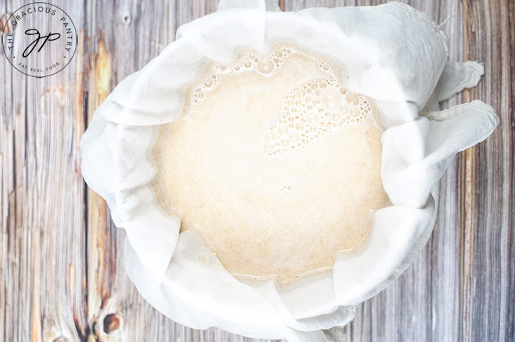 Oat milk sitting in a cheesecloth draped over a large bowl.