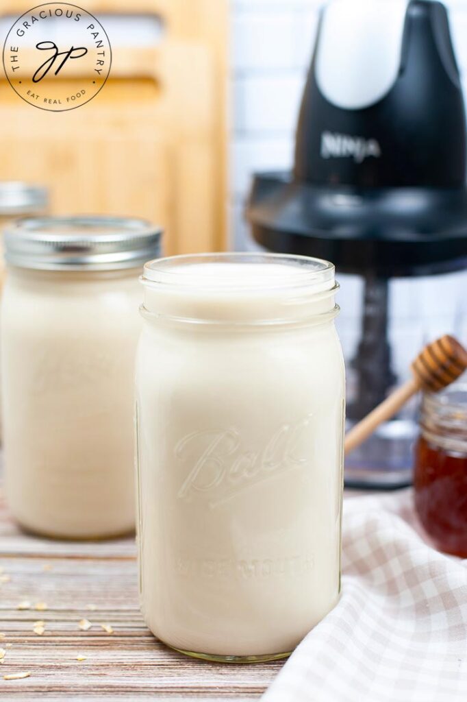 Three canning jars of oat milk stand in a row with a blender sitting behind them.