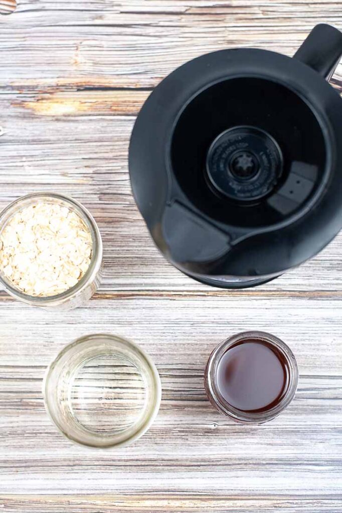 An overhead shot looking down into jars of individual oat milk ingredients sitting next to a blender.