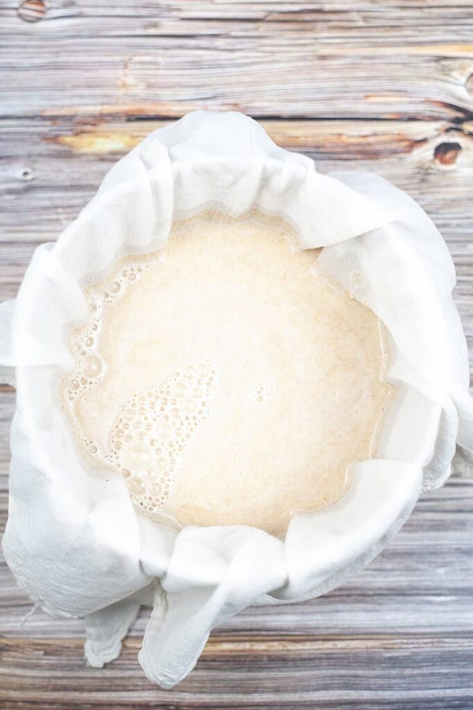 An overhead shot looking down into a cheesecloth-lined bowl filled with just blended oat milk.