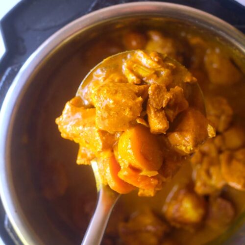 A close up of a ladle filled with Jamaican Curry Chicken.