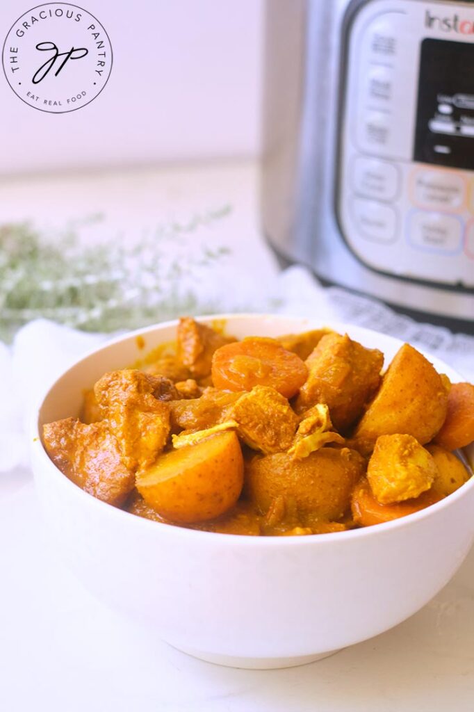 A white bowl filled with Jamaican Curry Chicken sits in front of an Instant Pot.