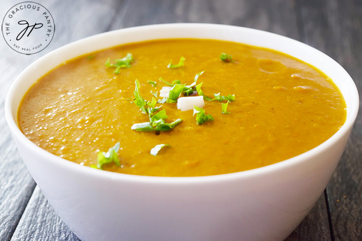 A white bowl filled with Kabocha Squash Soup and garnished with onion pieces and fresh herbs.