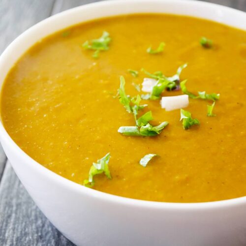A white bowl filled with Kabocha Squash Soup, sits on a gray background.