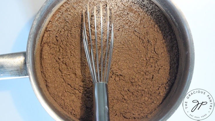 A small, stainless still pot with Protein Peppermint Mocha Creamer Recipe ingredients in it. A whisk rests in the pot.