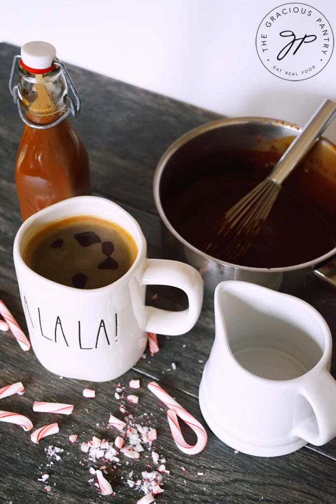 An overhead shot looking down into a mug of coffee, a pot of Protein Peppermint Mocha Creamer, and a small white pitcher and a capped bottle filled with the creamer.