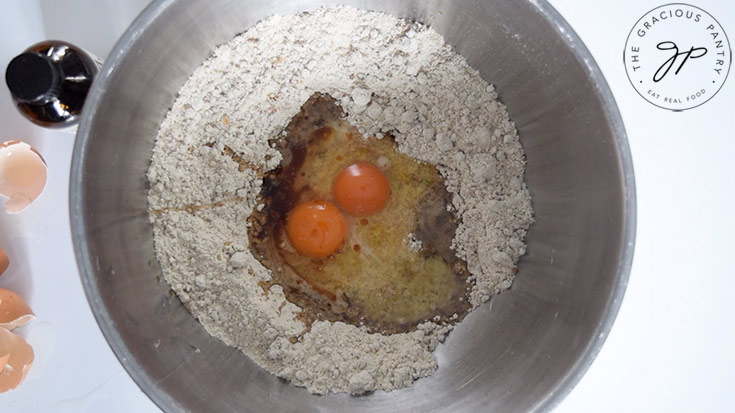Eggs and other wet ingredients being added to a flour mixture in a mixing bowl.