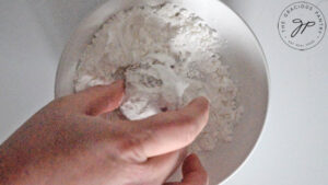 A Pfeffernusse Cookie being rolled in powdered sweetener.