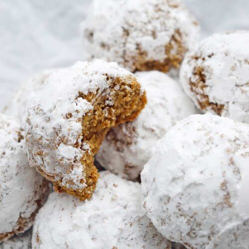 A pile of Pfeffernusse Cookies sitting on white parchment. A bite is missing from one of them.