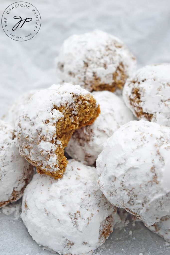 A pile of Pfeffernusse Cookies sitting on white parchment. A bite is missing from one of them.