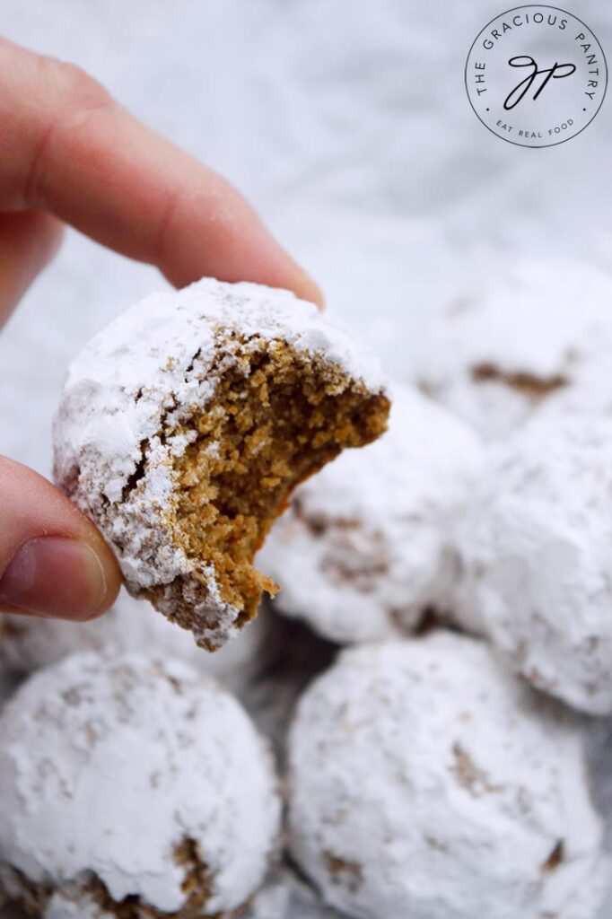 Hand holding up a single Pfeffernusse Cookie with a bite taken from it.