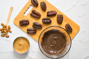 Melted chocolate in a small, glass bowl sits on a cutting board next to pitted dates.